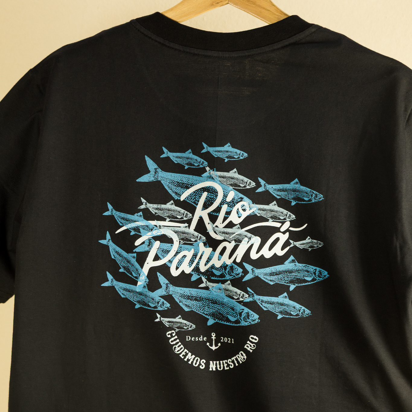 Remera negra de manga corta 100% algodón. Estampa dorso en serigrafía artesanal: cardumen de sábalos en azul y blanco rodeando el texto Río Paraná. Leyenda Cuidemos Nuestro Río con ancla. Ropa de diseño urbano, marca Río Paraná.